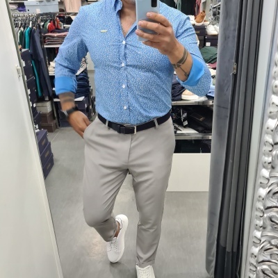 Homem com camisa azul claro e calças bege cinzentas em loja de roupas