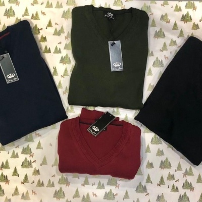 Quatro camisas de malha em azul escuro, verde, preto e vermelho sobre tecido com padrão de árvores