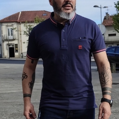 Polo masculino azul escuro com detalhes vermelhos e bolso frontal usado por homem ao ar livre