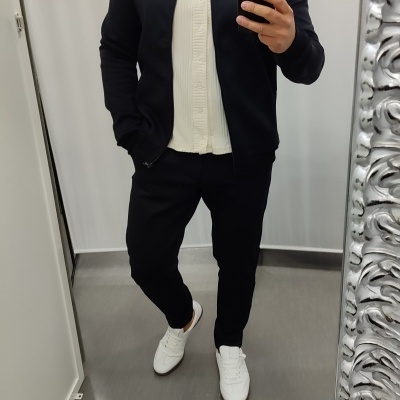 Homem em roupa casual preta e bege a tirar selfie em espelho interior.