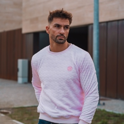 Homem veste sweatshirt rosa claro acolchoada com calças de ganga em cenário urbano