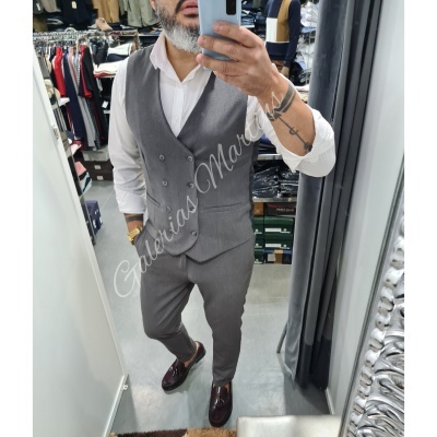 Homem em loja vestindo colete e calças cinza escuro, camisa branca e sapatos castanhos