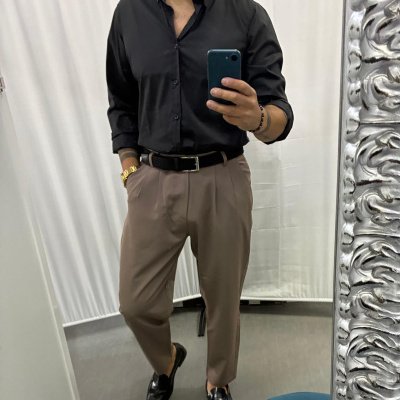 Homem com camisa preta, calças bege, cinto preto e sapatos pretos a tirar selfie num espelho