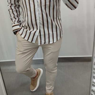 Homem a usar camisa riscada branca com calças bege e sapatilhas castanhas num espaço interior