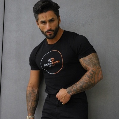 Homem com t-shirt preta estampada e calças pretas num fundo cinza