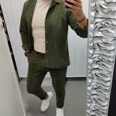 Pessoa em roupa verde com t-shirt bege e ténis brancos em frente a espelho prateado