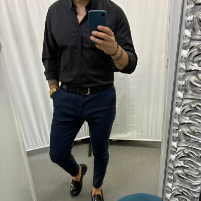 Homem com camisa preta e calças azuis escuras a tirar selfie num espelho