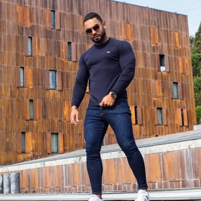 Homem com t-shirt azul escura, jeans e ténis brancos em ambiente urbano