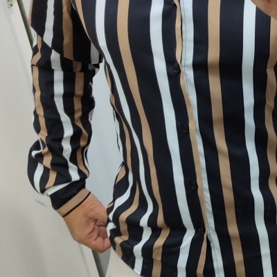 Camisa de riscas verticais preto, branco e castanho com calças claras e sapatos castanhos