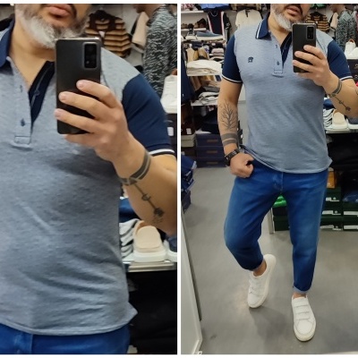 Homem a vestir polo azul e calças azuis, a tirar selfie num espelho numa loja.