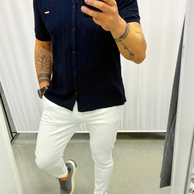 Homem a usar camisa preta, calças brancas e sapatilhas cinzentas em frente a espelho