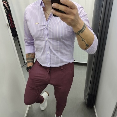 Homem com camisa lilás riscada, calças vinho tinto e sapatilhas brancas no provador