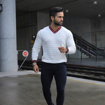 Homem com camisola branca de malha com riscas na gola e calças e sapatos pretos numa estação ferroviária