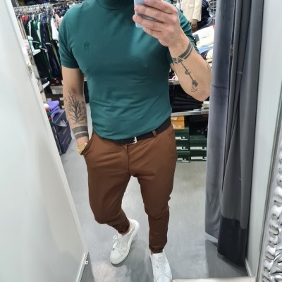 Homem vestido com t-shirt verde escuro, calças castanhas e sapatilhas brancas numa loja de roupa