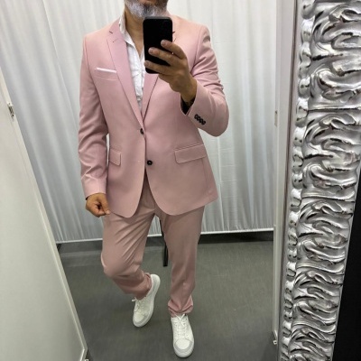 Homem com fato rosa claro, camisa branca e sapatilhas brancas posando em espelho com moldura prateada