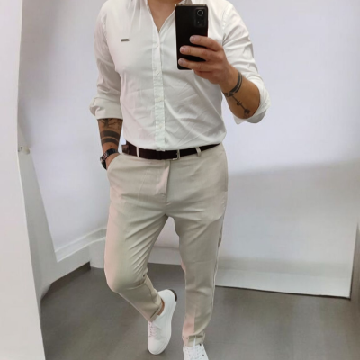 Homem com camisa branca, calças bege, cinto castanho e sapatilhas brancas em frente a espelho