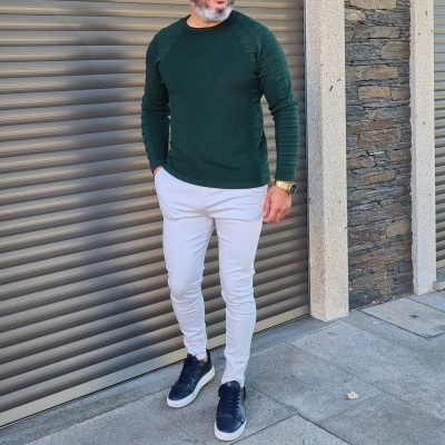 Homem com camisola verde, calças bege e sapatilhas pretas em ambiente urbano