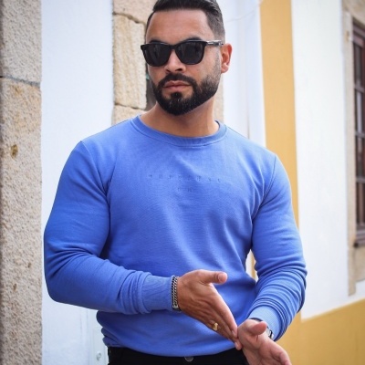 Homem com sweatshirt azul de manga comprida e óculos escuros em ambiente urbano