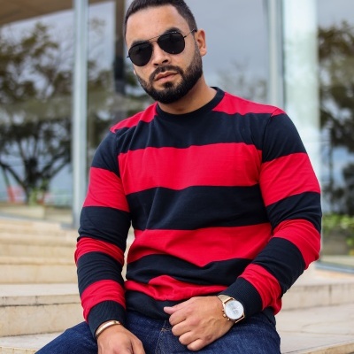 homem sentado com camisola riscada vermelha e preta, óculos escuros e relógio