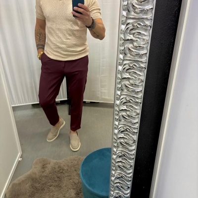 Homem com camisa bege, calças borgonha e sapatos bege a tirar selfie em espelho com moldura prateada.