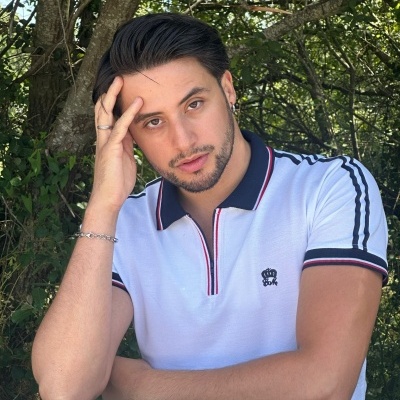 Homem com camisola branca com riscas pretas e vermelhas sentado ao ar livre junto a mesa