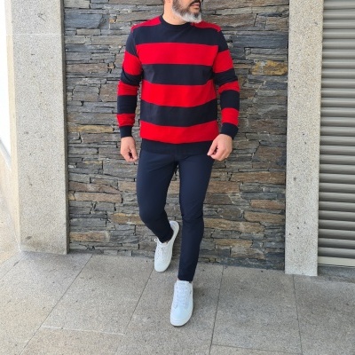 Homem com camisola de riscas vermelhas e pretas, calças azuis escuras e sapatilhas brancas
