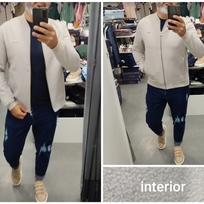 Homem a vestir casaco bege, calças azuis rasgadas e ténis bege, em loja de roupas com texto 'interior' no espelho.