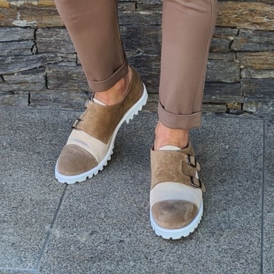Sapatos castanhos e bege com solado branco usados com calças castanhas em piso de pedra cinzenta