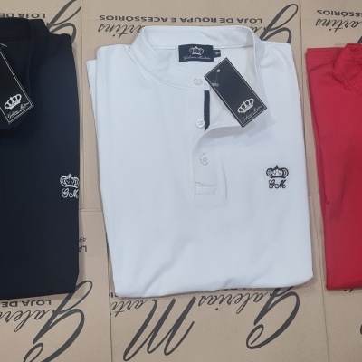 Três polos masculinos dobrados preto, branco e vermelho com logo bordado e etiquetas numa superfície de caixas de papelão.