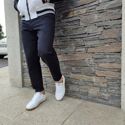 Pessoa com calças pretas e ténis brancos junto a parede de pedra