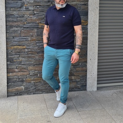 Homem com camisa polo azul escura, calças chinos azul claro e ténis brancos