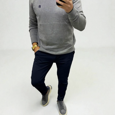 Homem com camisola cinza e calças pretas a tirar selfie com telemóvel preto