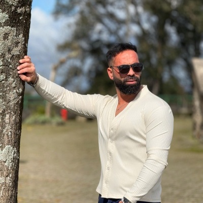 Homem com camisa branca canelada e óculos de sol ao ar livre junto a árvore