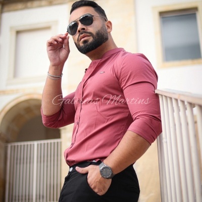 Homem com camisa vermelha e óculos de sol pretos em ambiente urbano.