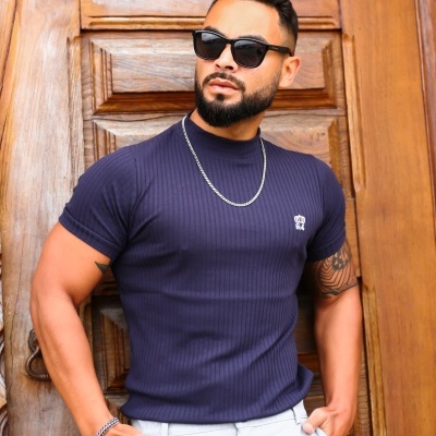 Homem com camisa azul escuro canelada e óculos escuros em frente a porta de madeira