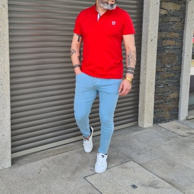 Homem com polo vermelha, calças azuis claras e sapatilhas brancas em frente a porta de rolo cinzenta