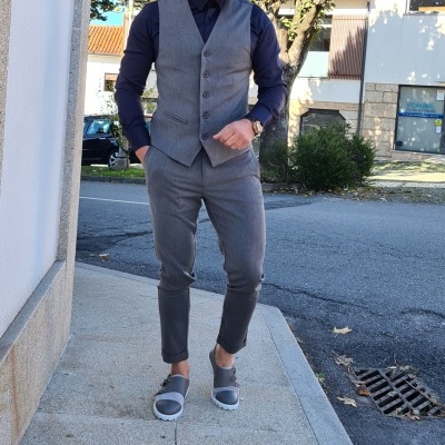 Homem vestido com colete e calças cinza e camisa azul escura numa rua