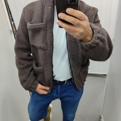 Pessoa com casaco castanho felpudo e calças jeans azuis em frente a espelho