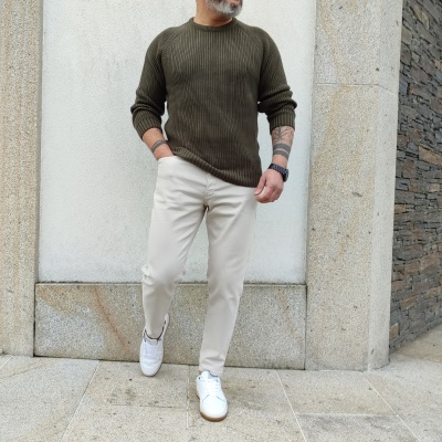 Homem com camisola verde-oliva de malha e calças claras em ambiente exterior