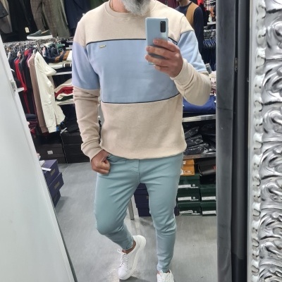 Homem com sweatshirt bege e azul, calças azul claro e sapatilhas brancas numa loja de roupa