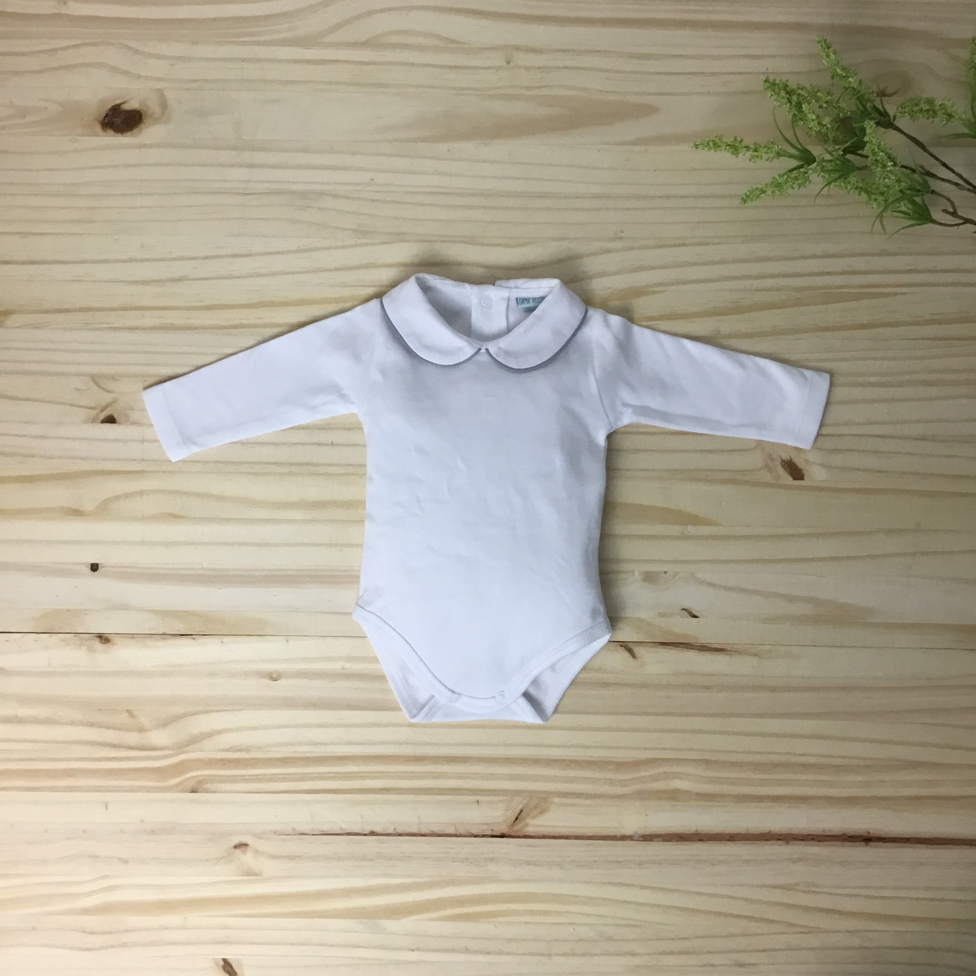 Body de bebé branco com mangas compridas e gola redonda sobre madeira clara