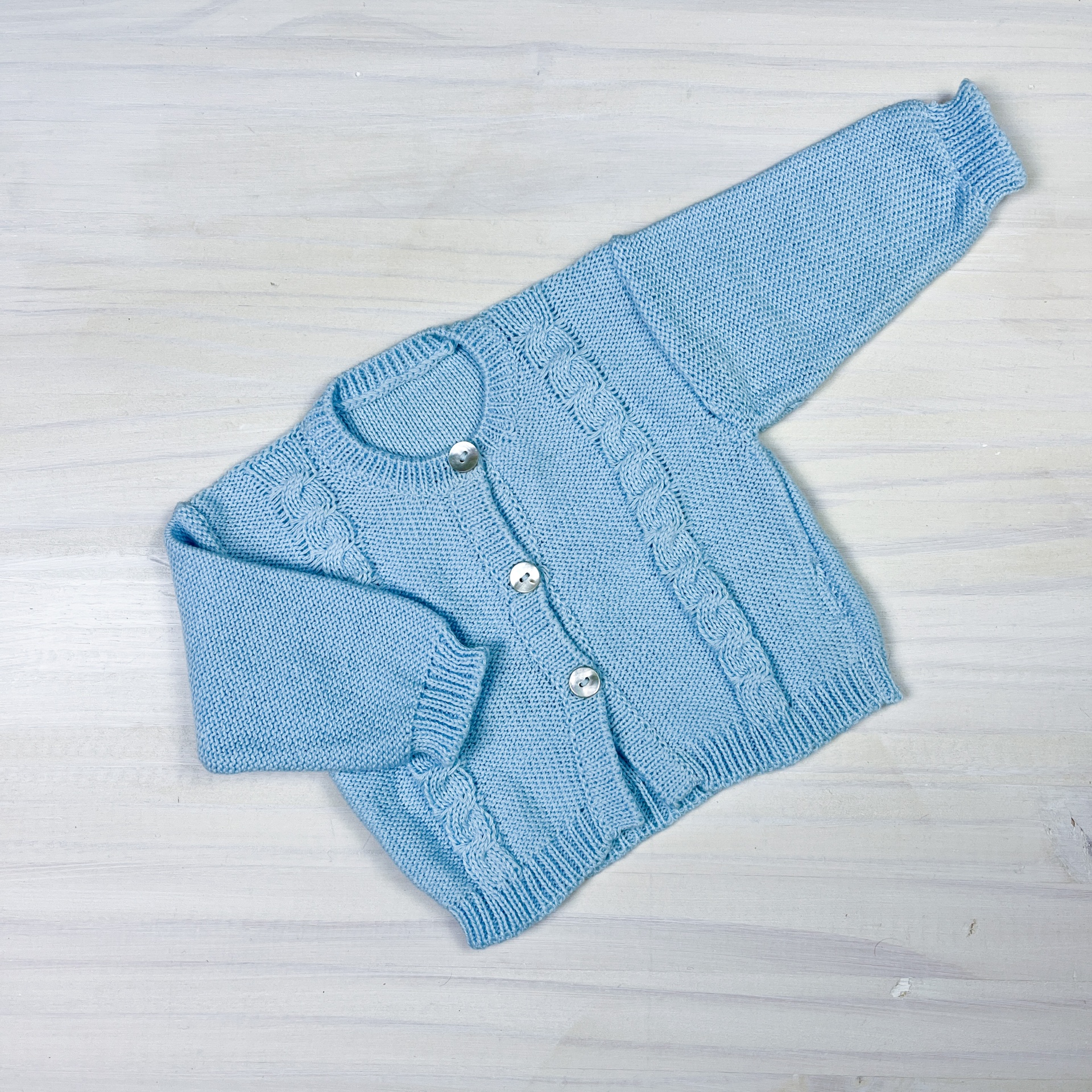 Casaco azul claro de malha para bebé com botões brancos e padrão de tranças