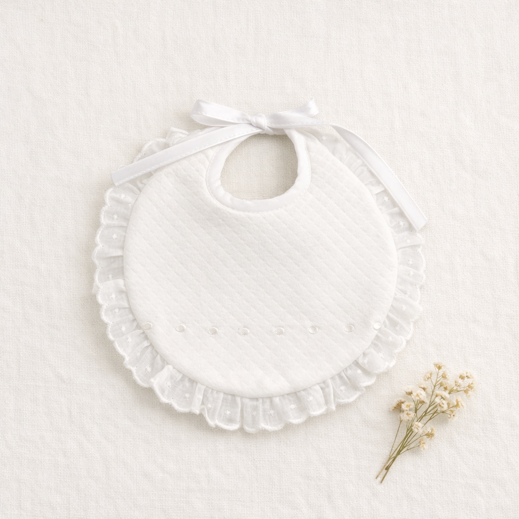 Babete branco acolchoado com renda e laço sobre tecido branco