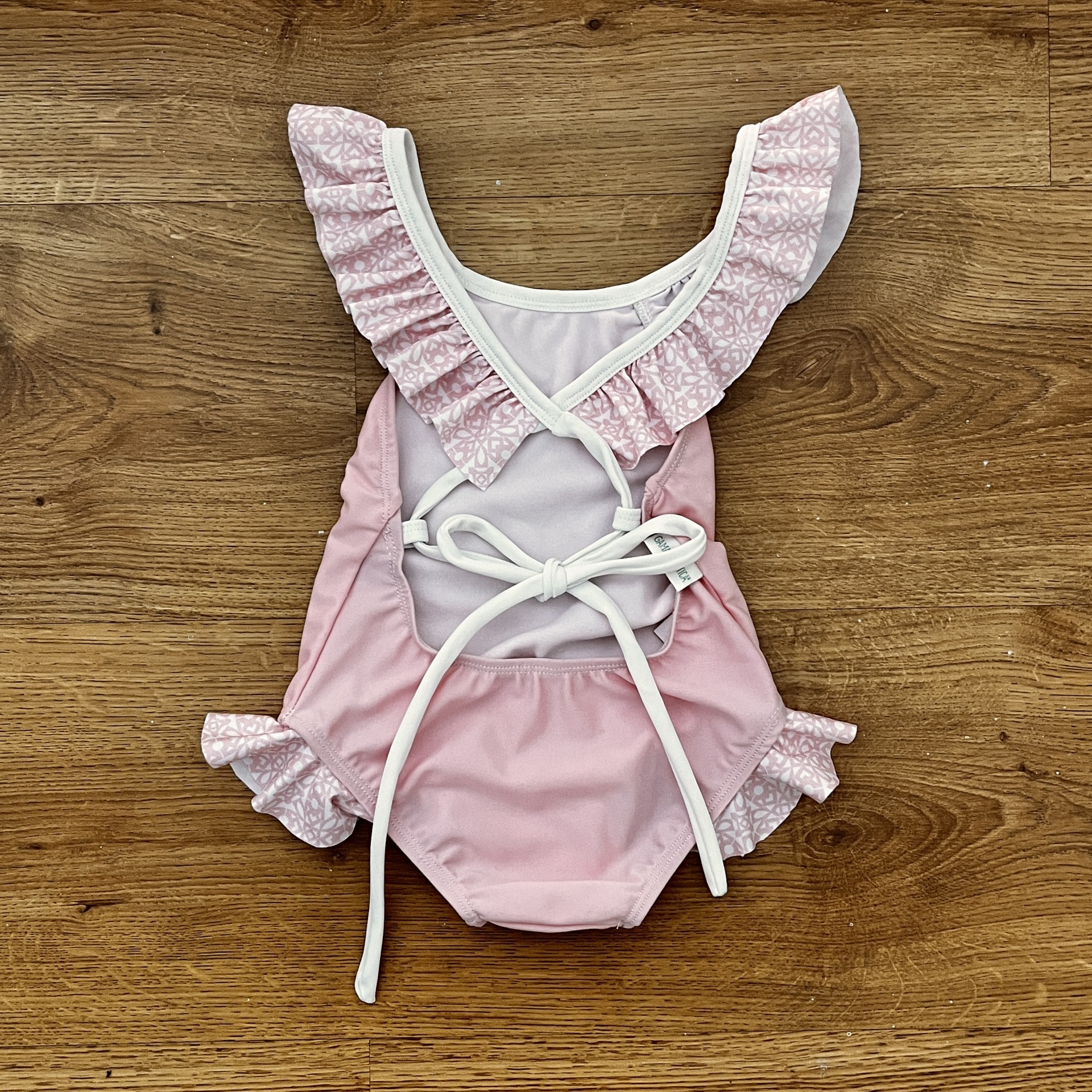 Fato de banho de bebé rosa e branco com folhos e fitas para amarrar sobre madeira