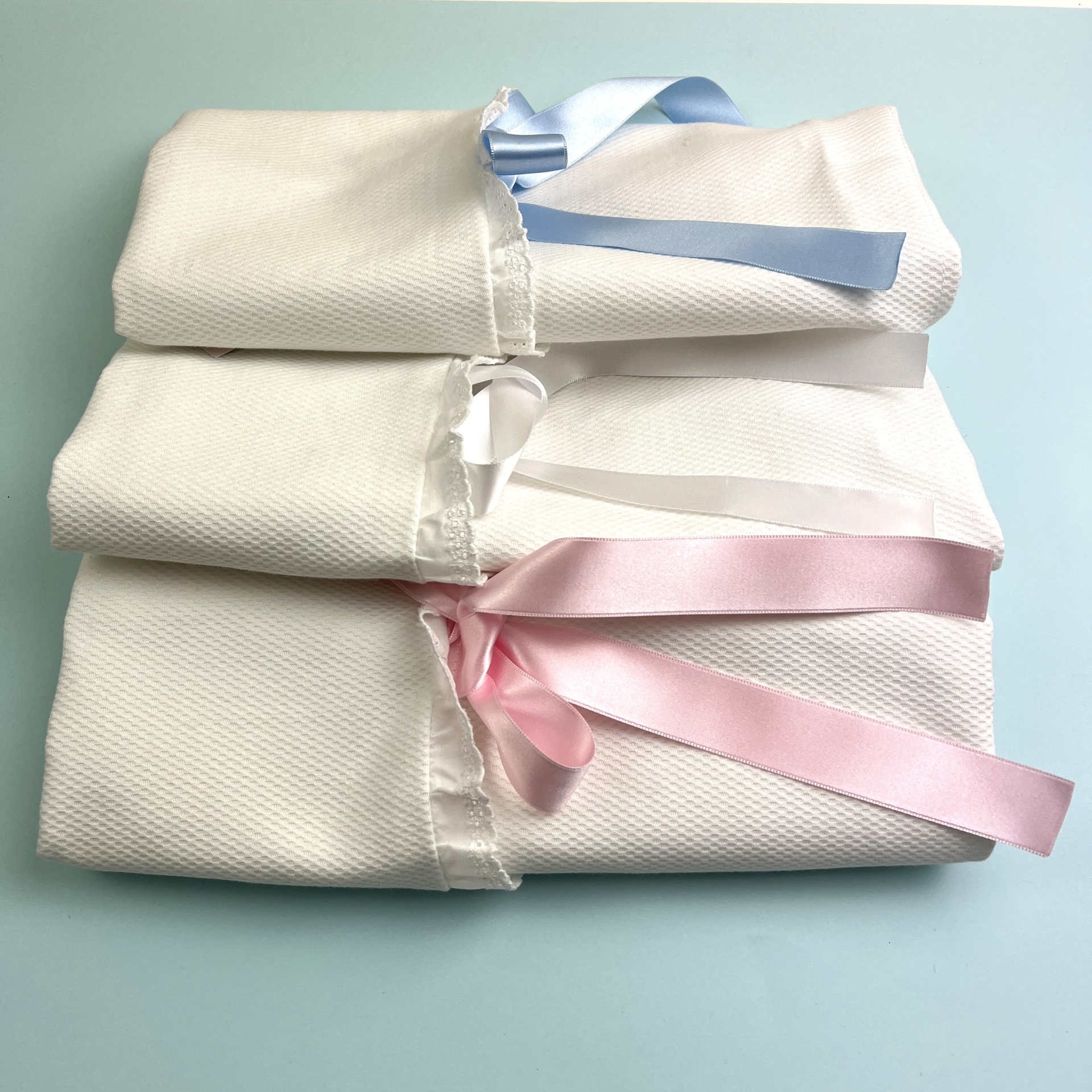 Três sacos de tecido branco com fitas azul, branca e rosa amarradas