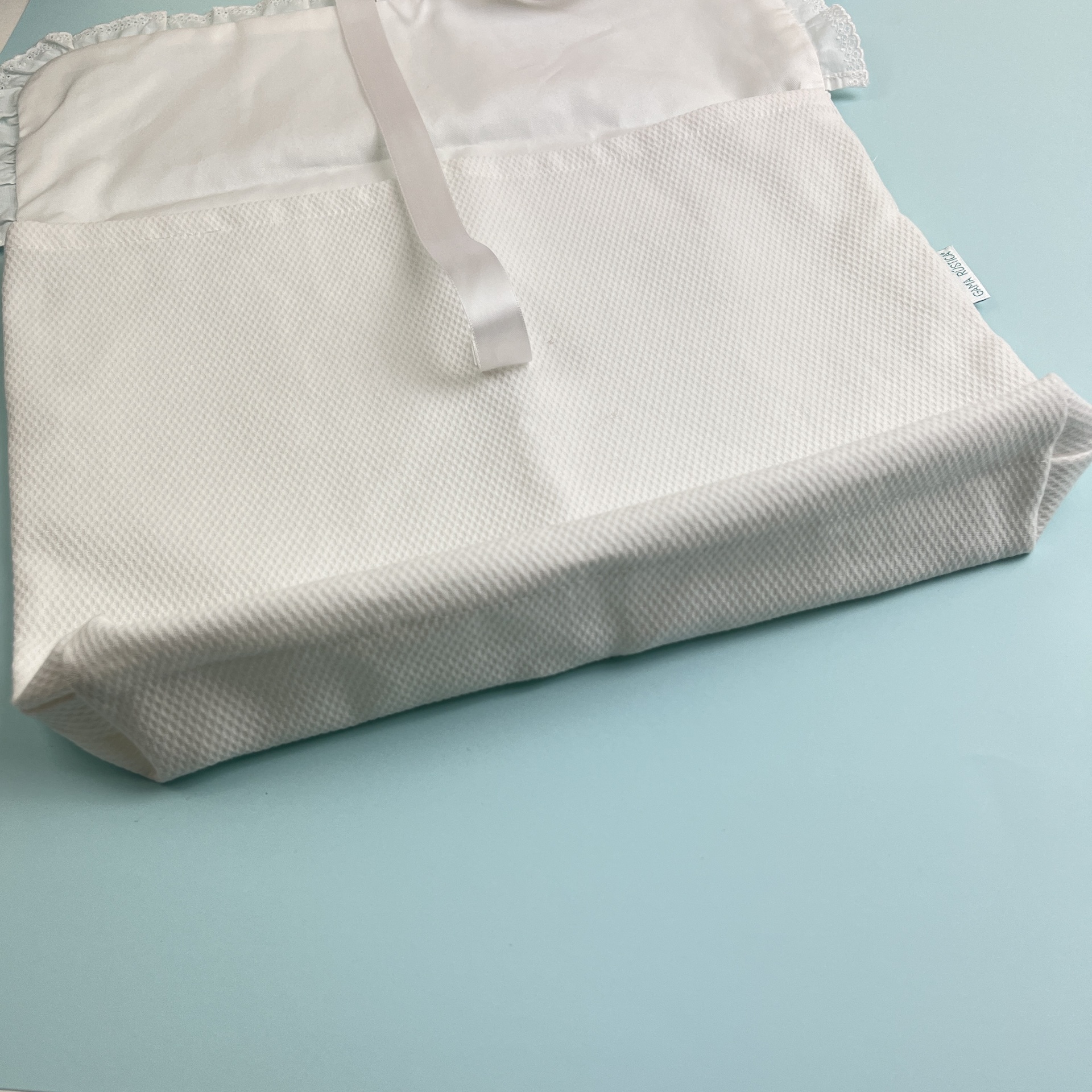 Saco branco de tecido com textura e alça sobre superfície azul clara
