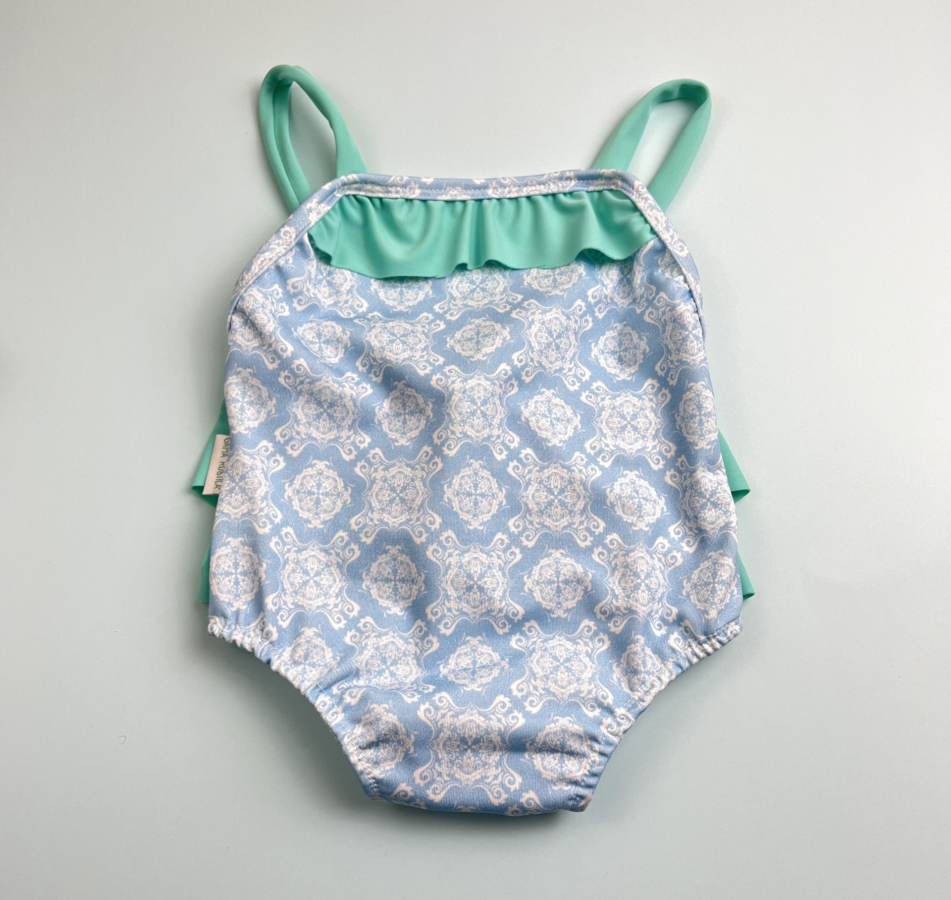 Fato de banho de criança azul e verde com padrão branco sobre fundo cinza claro