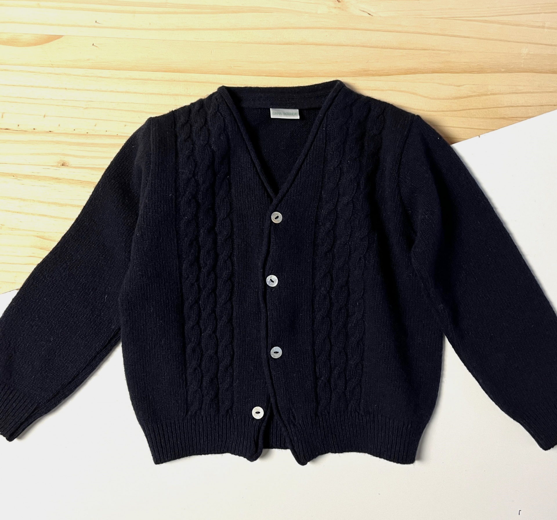 Casaco de malha preto com botões brancos e padrão de trança