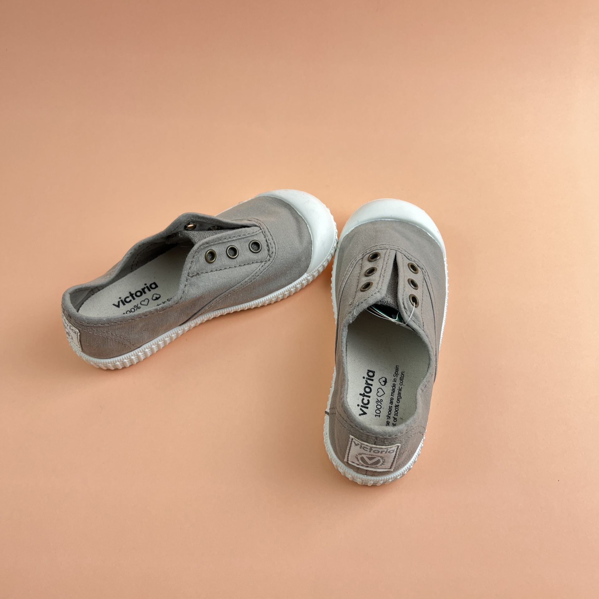 Sapatos infantis cinza claro com sola branca em fundo cor de pêssego