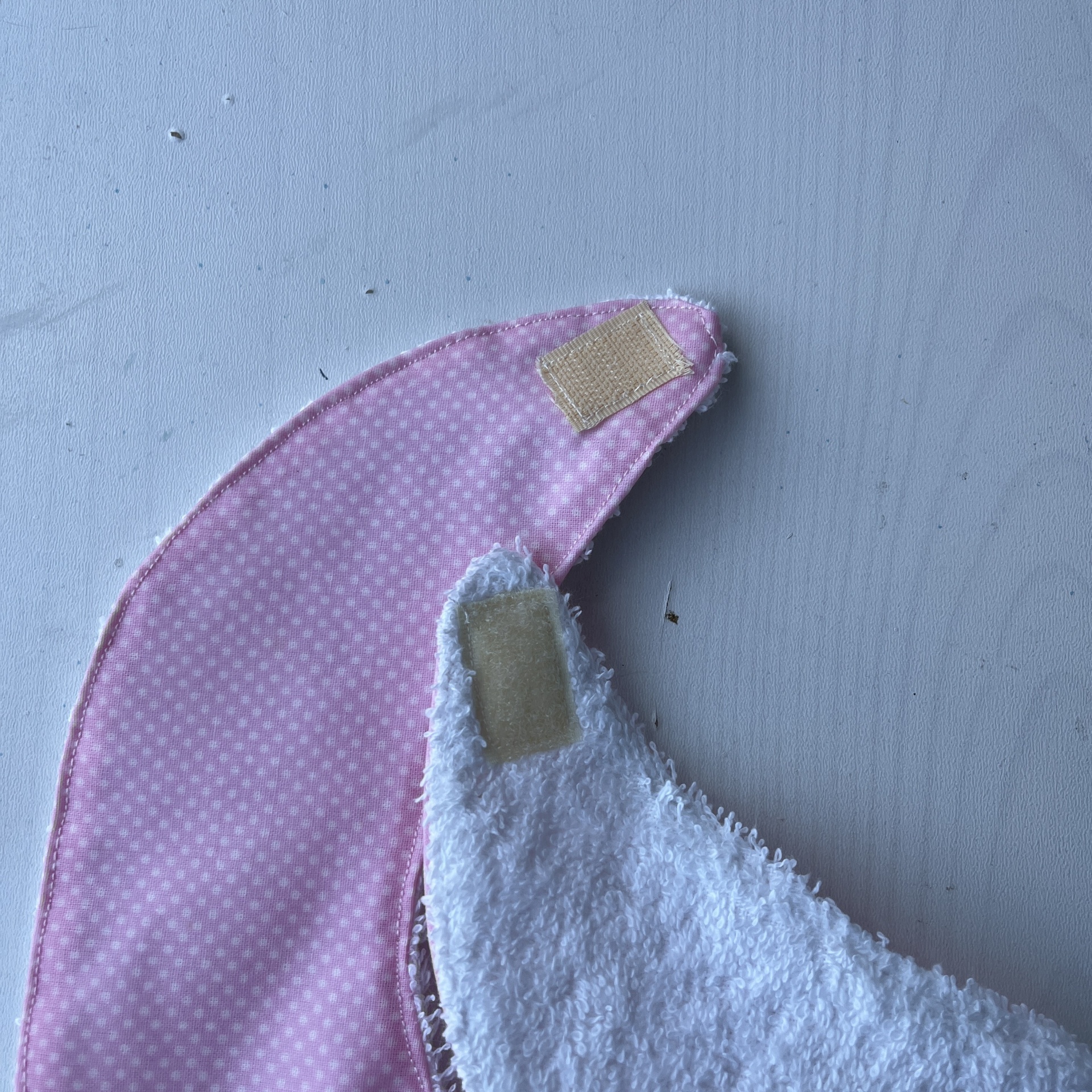 Dois babetes, um rosa com pontos e outro branco felpudo, ambos com velcro